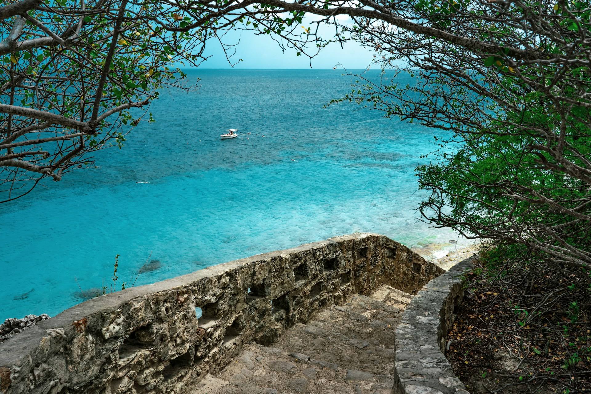 Escalera de piedra de 1000 Steps, en Bonaire, que baja entre árboles hacia un mar turquesa con una lancha frente a la costa