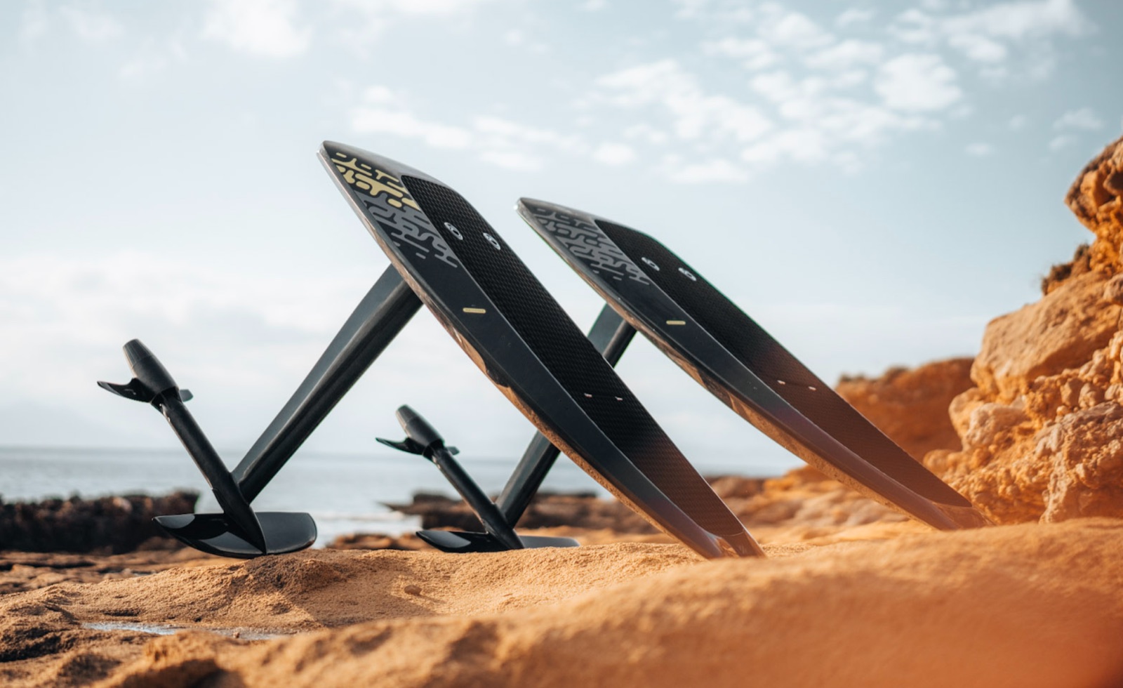 Deux planches carbone Audi e-tron foil avec mât et aile posées sur un rivage rocheux