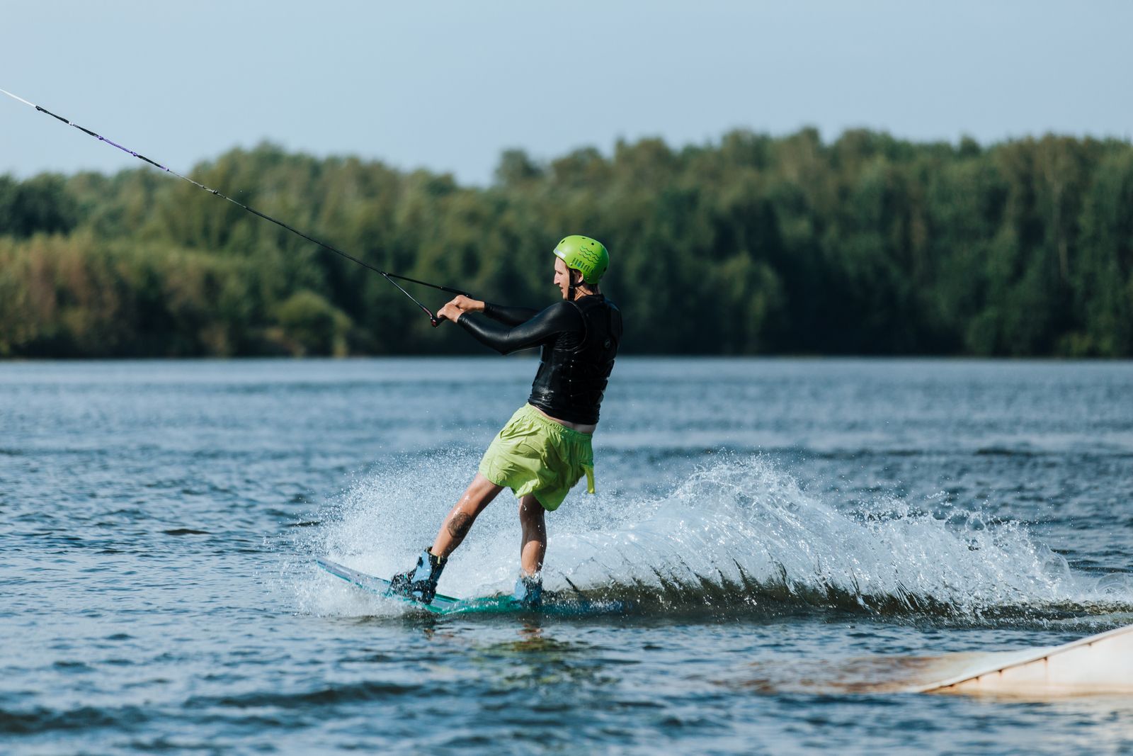 Wakeboarder met groene helm bij een schans in een kabelbaan, met loofbos op de oever; geen efoil en niet in Roermond (beeld ter illustratie)
