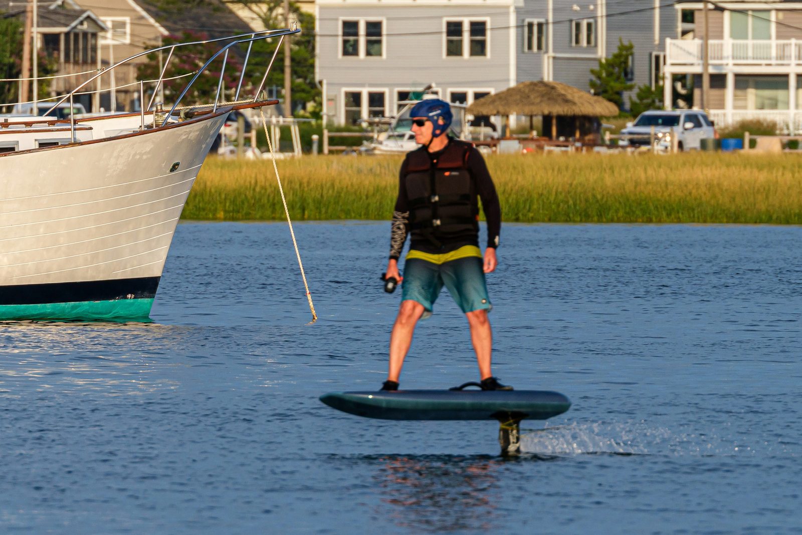 Rider in a helmet and impact vest standing on an eFoil just above the water, remote in hand