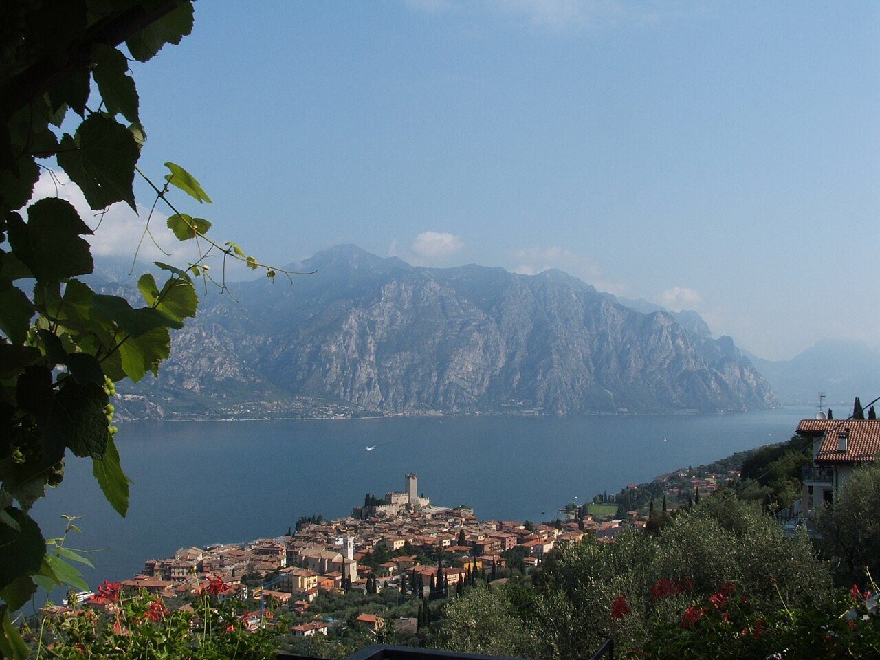 Malcesine seen from the hillside above, its castle tower on the shore of Lake Garda and the mountains of the western shore across the water