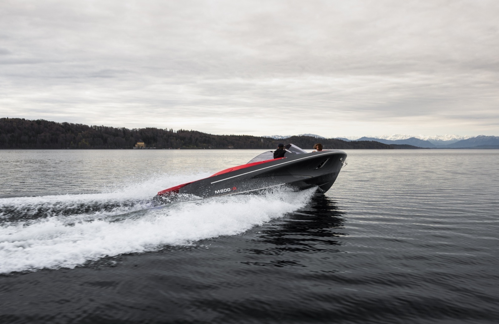 A black and red ABT | Marian M 800-R running fast with a bow wave against a mountain backdrop