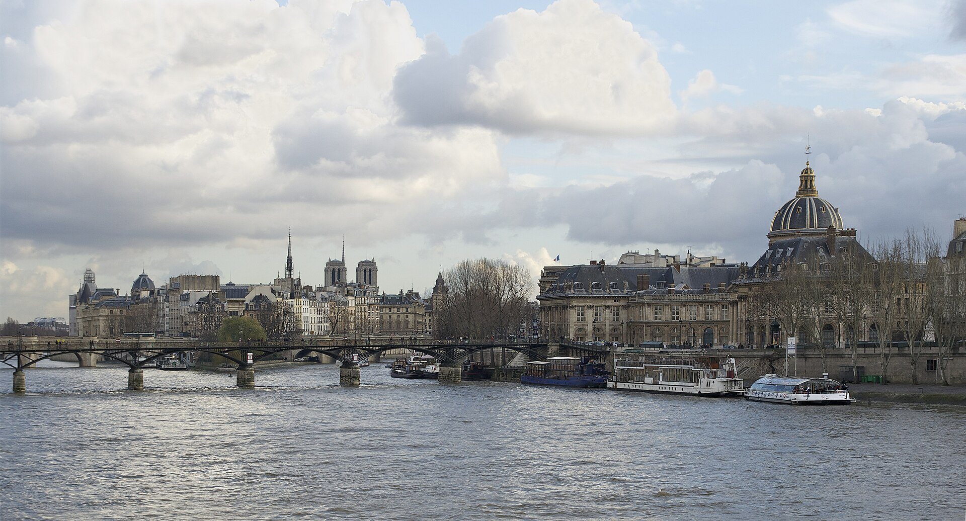 The Seine at the pont des Arts under a cloudy sky, with the dome of the Institut de France and Notre-Dame beyond